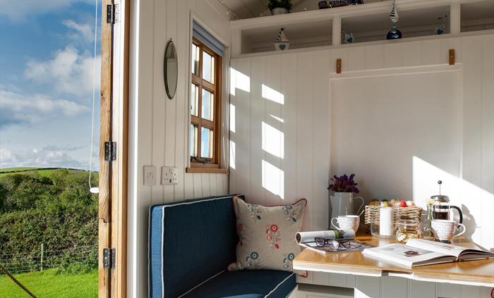 This shows the table and seating in the hut.  It is very bright and sunny inside, the table is has coffee and biscuits, perfect to sit and read a maga